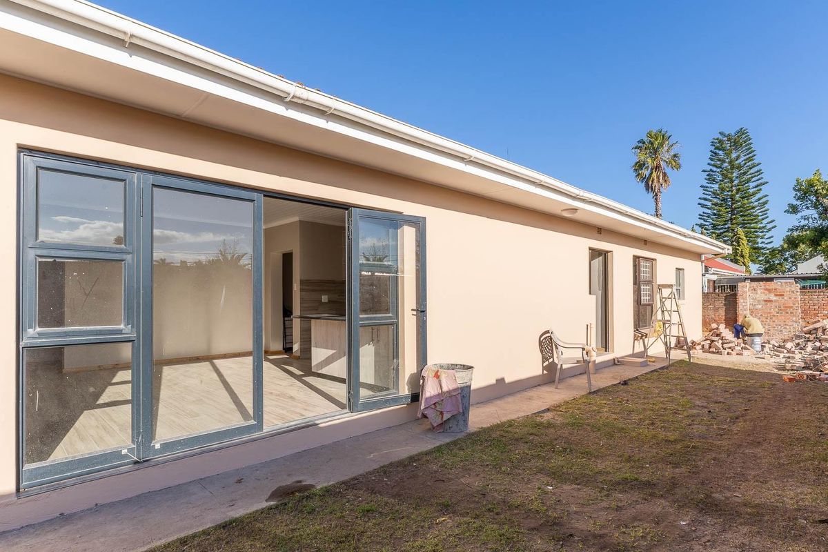 Rear view of the property featuring a paved walkway, modern aluminium sliding doors, and an open-plan interior space with a kitchen visible.