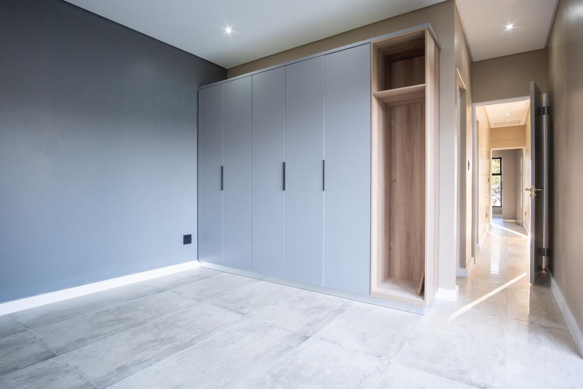 A modern bedroom featuring built-in floor-to-ceiling cabinetry with a mix of grey doors and open wood-toned shelving, complemented by large format floor tiles.