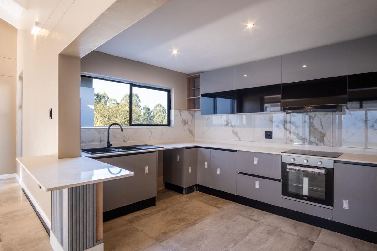 Modern kitchen featuring sleek grey cabinetry, marble-look splashbacks, stone countertops, integrated oven, and a black sink with a contemporary mixer tap.