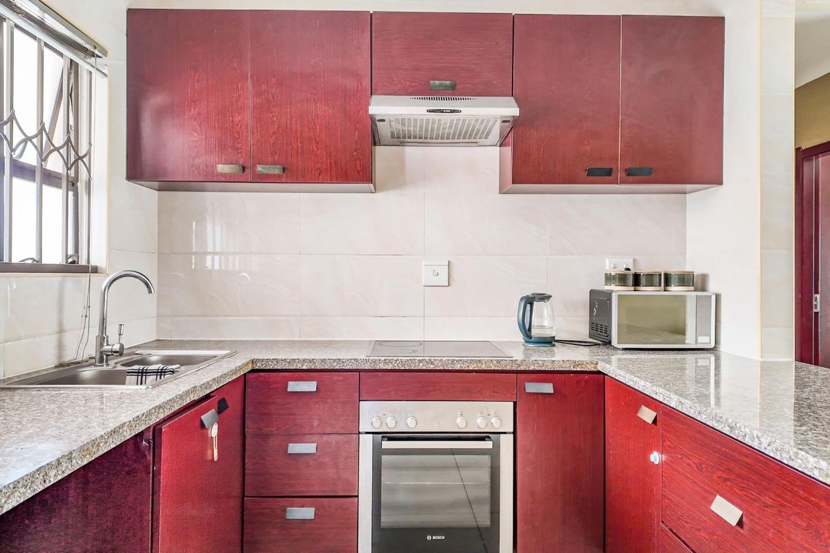 A functional kitchen featuring dark wood cabinetry, granite countertops, a built-in oven, electric hob, extractor fan, and a stainless steel sink.