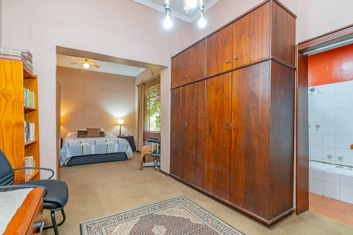 A spacious bedroom featuring built-in wooden cabinetry and an adjoining en-suite bathroom with a bathtub and shower combination.