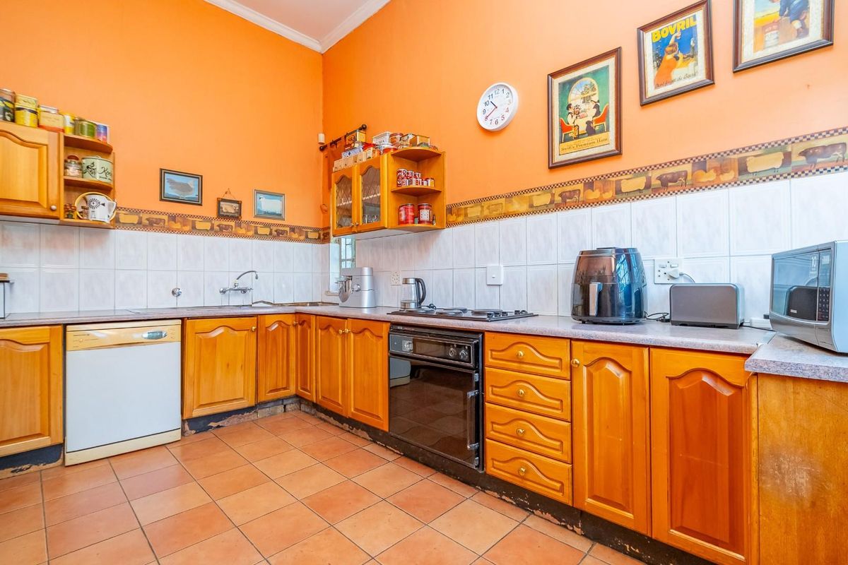 A dated kitchen featuring wooden cabinetry, tiled flooring, and a tiled backsplash with a decorative border.