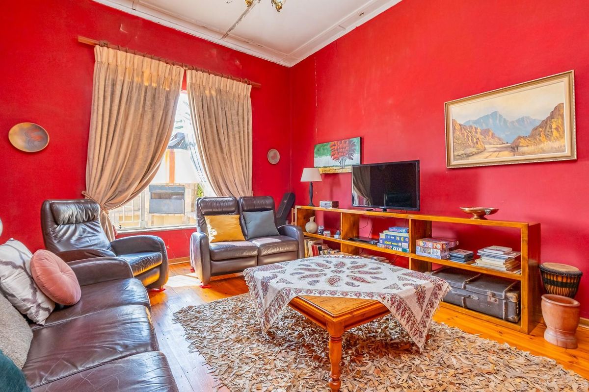 A living room featuring original timber flooring, high ceilings with decorative cornicing, and large windows allowing natural light.