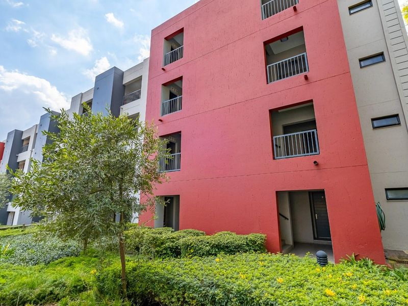 Exterior view of a modern multi-story townhouse complex featuring red and grey facade finishes with integrated balconies and landscaped garden surrounds.