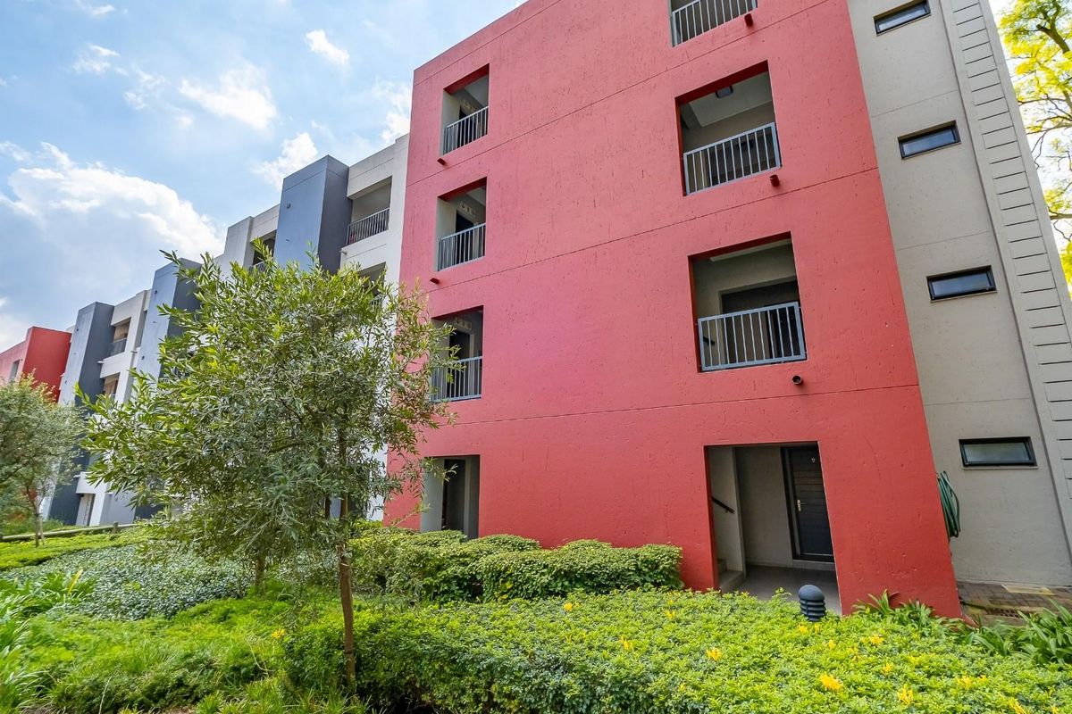 Exterior view of a modern multi-story townhouse complex featuring red and grey facade finishes with integrated balconies and landscaped garden surrounds.