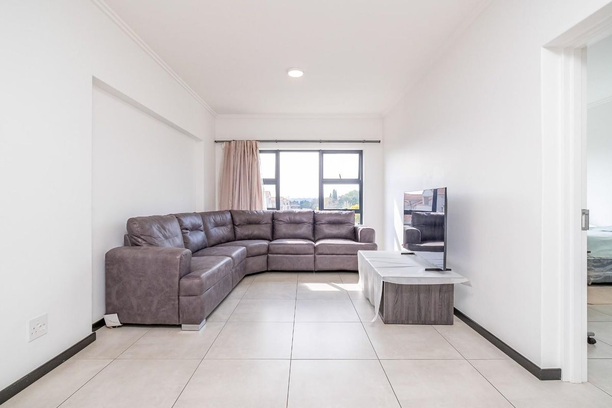 A bright and spacious living room featuring large windows, neutral tiled flooring, and recessed ceiling lighting, offering a clean and modern aesthetic.