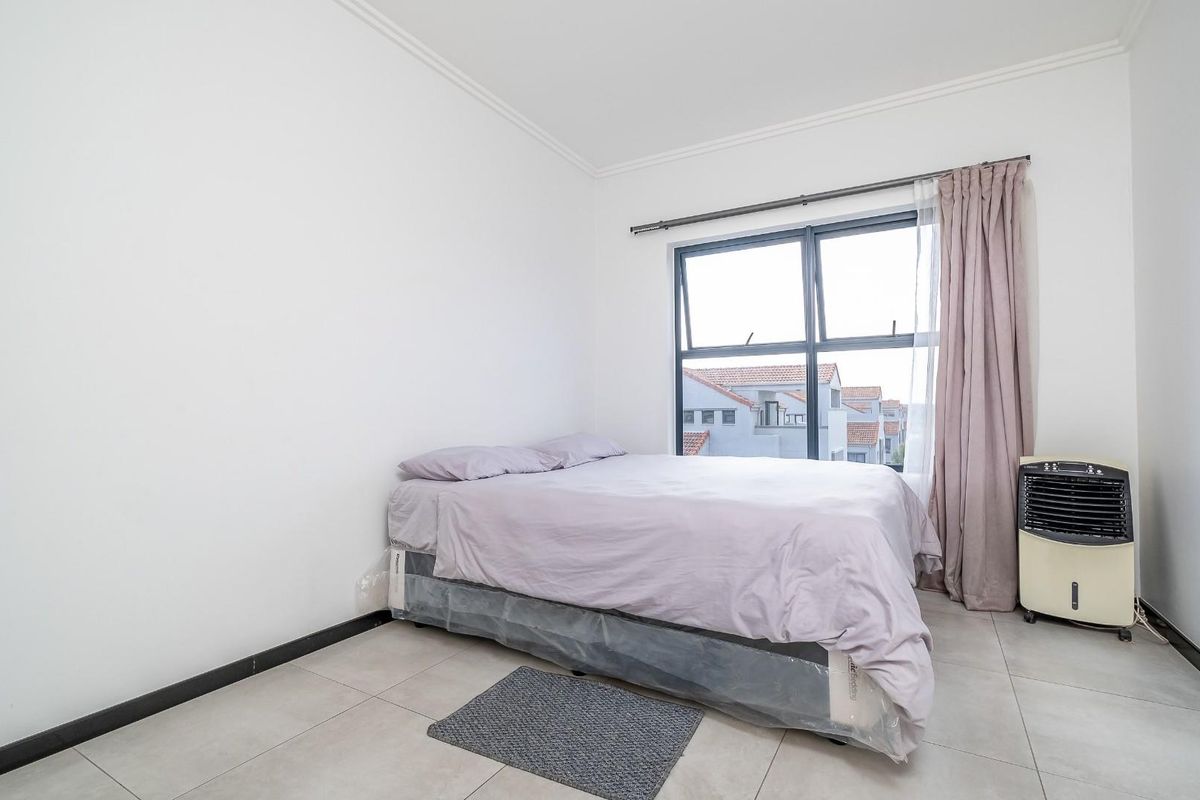 A bright bedroom featuring neutral tiled flooring, white walls, and a large window with curtain tracks.