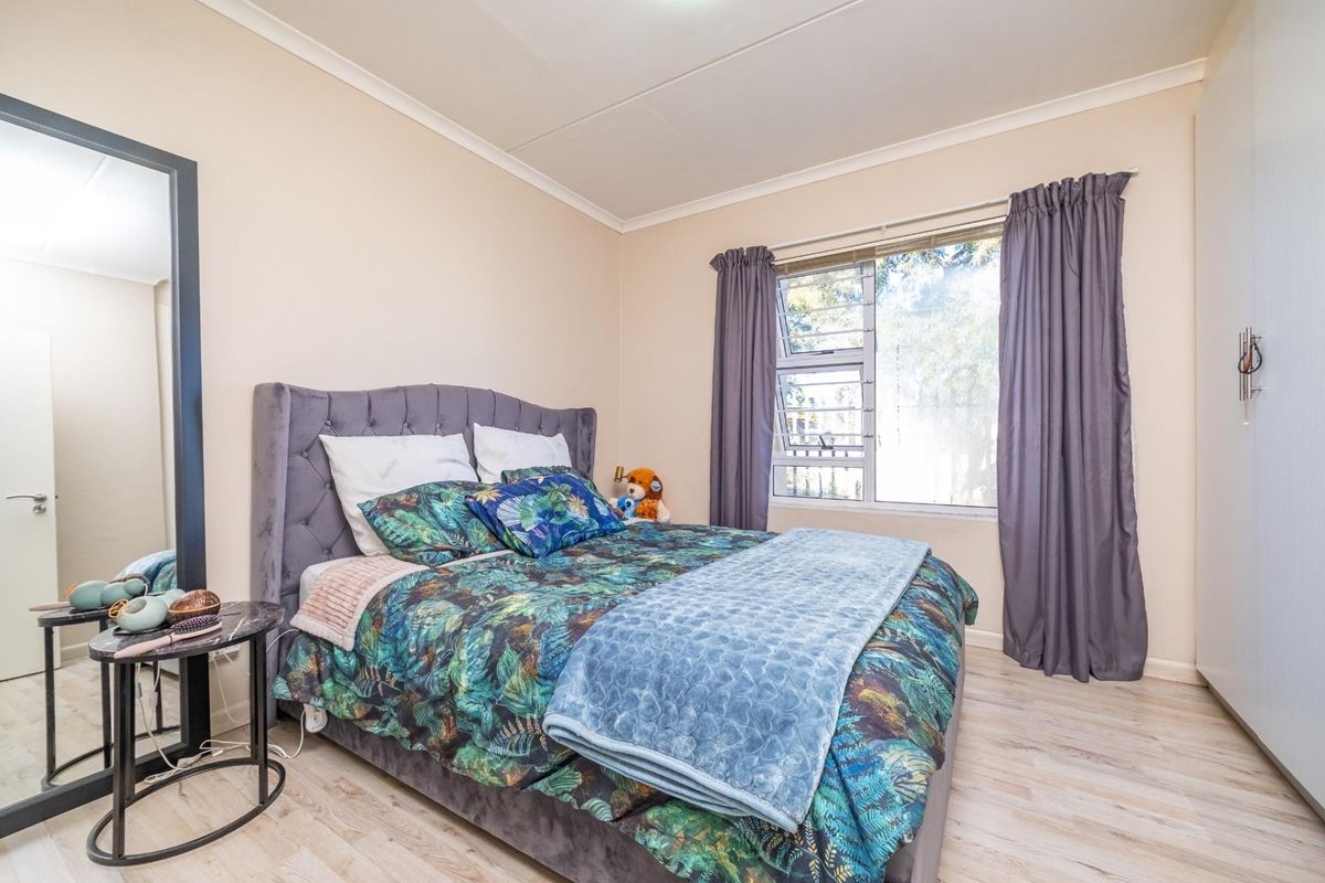 A well-maintained bedroom featuring light wood-look flooring, built-in cupboards, and a large window allowing for natural light.