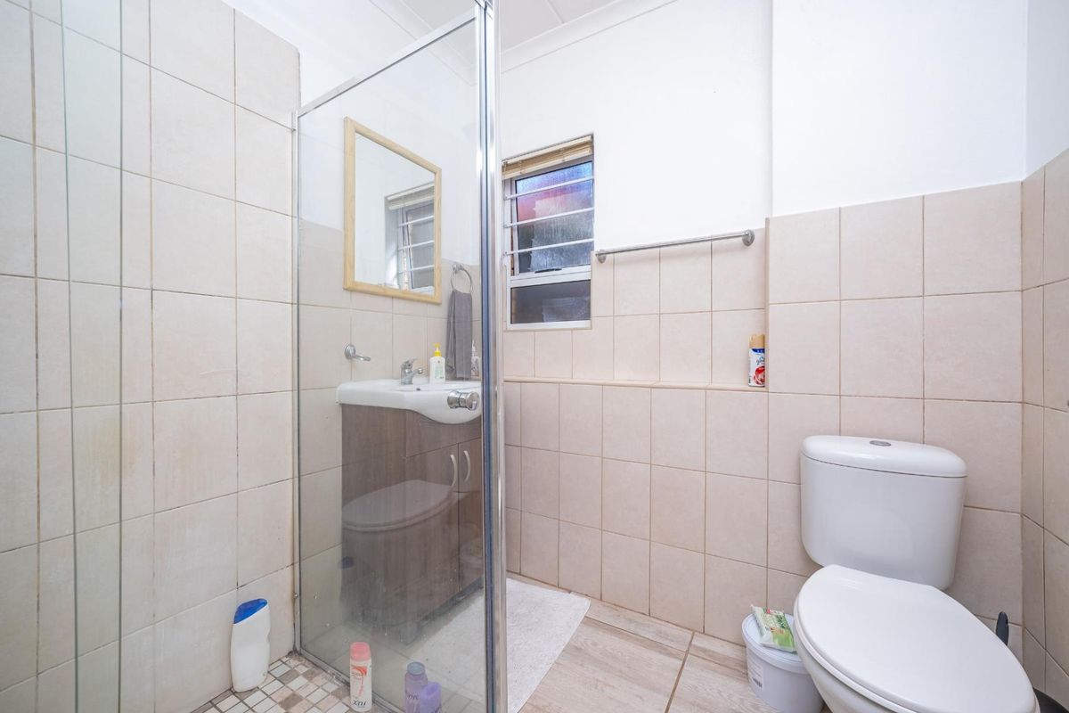 A functional bathroom featuring a glass-enclosed shower, vanity cabinet with basin, and a standard toilet, finished with neutral wall tiling.