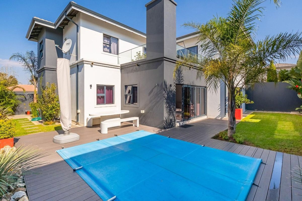 Rear view of the property featuring a swimming pool with a cover, composite decking, and a landscaped garden area.
