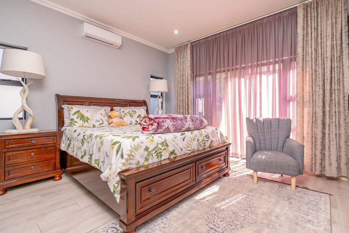 A well-maintained bedroom featuring light wood-look flooring, a wall-mounted air conditioning unit, and large sliding glass doors with floor-to-ceiling curtains.