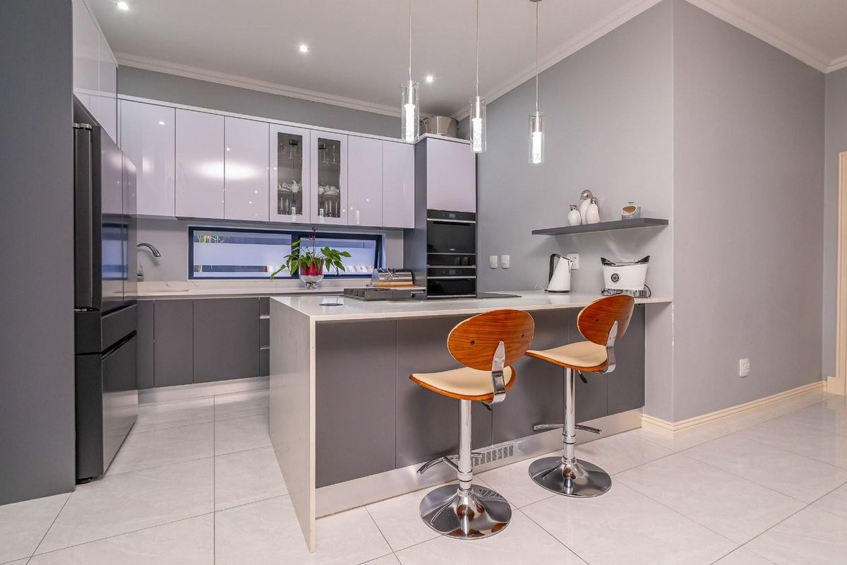 Modern kitchen featuring sleek two-tone cabinetry, a central island with breakfast bar seating, integrated oven, and high-quality tiled flooring.