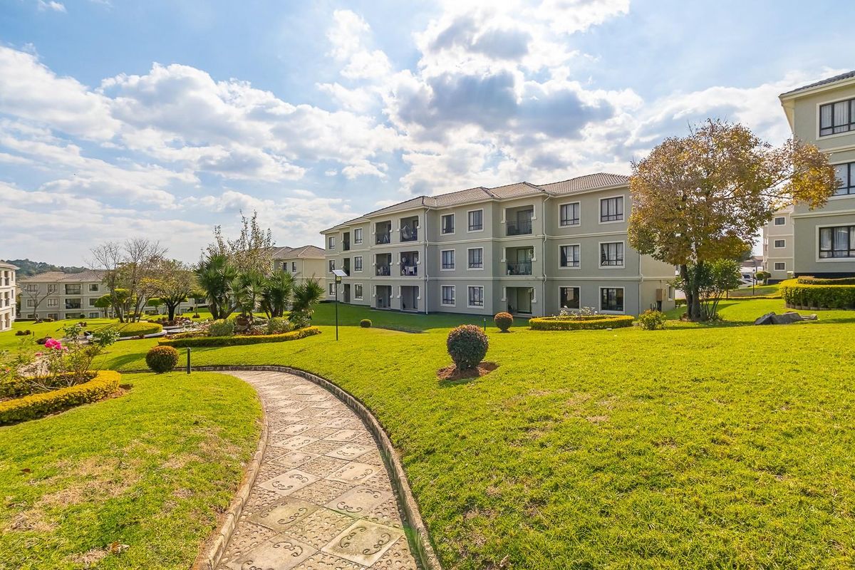 A view of the apartment complex exterior featuring well-maintained landscaped gardens and paved walkways between the residential buildings.