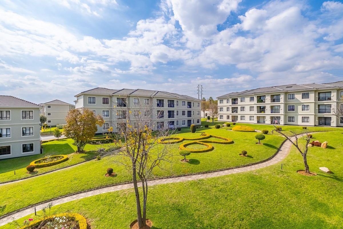 Aerial view of a well-maintained apartment complex featuring landscaped green spaces, manicured hedges, and paved pedestrian walkways between residential buildings.