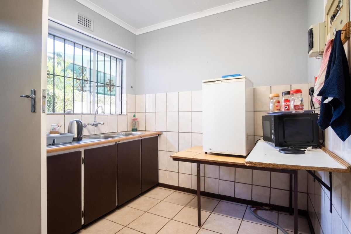A compact kitchenette featuring basic cabinetry, a stainless steel sink, and tiled splashbacks, suitable for a small office break area.