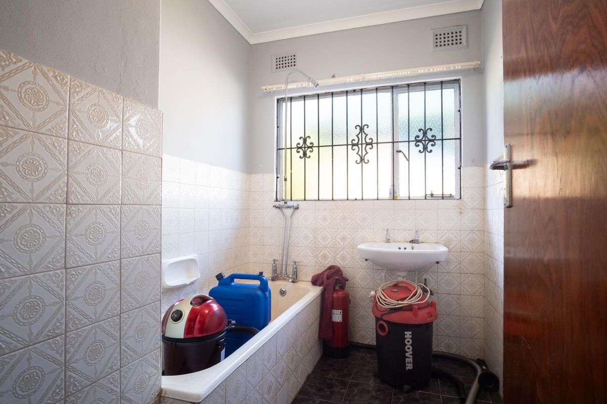 A functional bathroom featuring a bathtub, pedestal basin, and security bars on the window, currently used for storage.