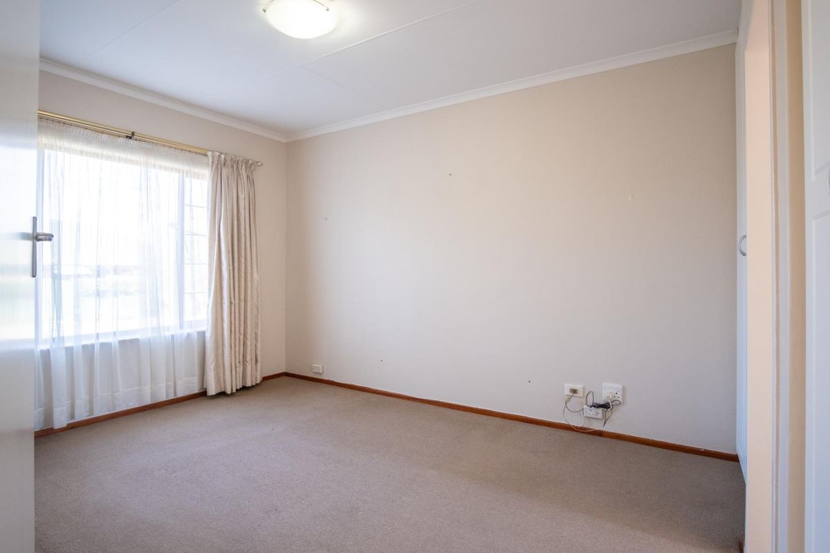 A neutral, empty bedroom featuring carpeted flooring, a large window with curtain tracks, and built-in cupboard space.