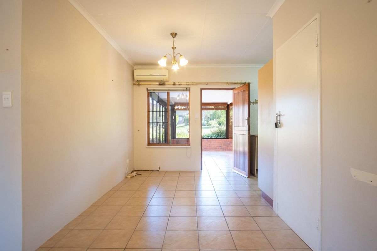 A bright, empty living area featuring tiled flooring, a wall-mounted air conditioning unit, and direct access to an outdoor patio space.