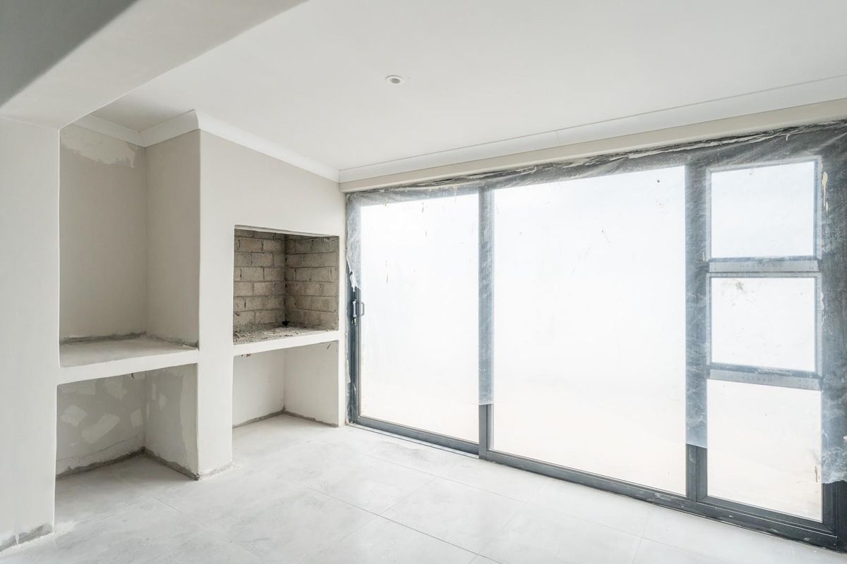 An unfinished living area featuring a built-in fireplace structure, large sliding glass doors, and tiled flooring, currently in a state of completion.