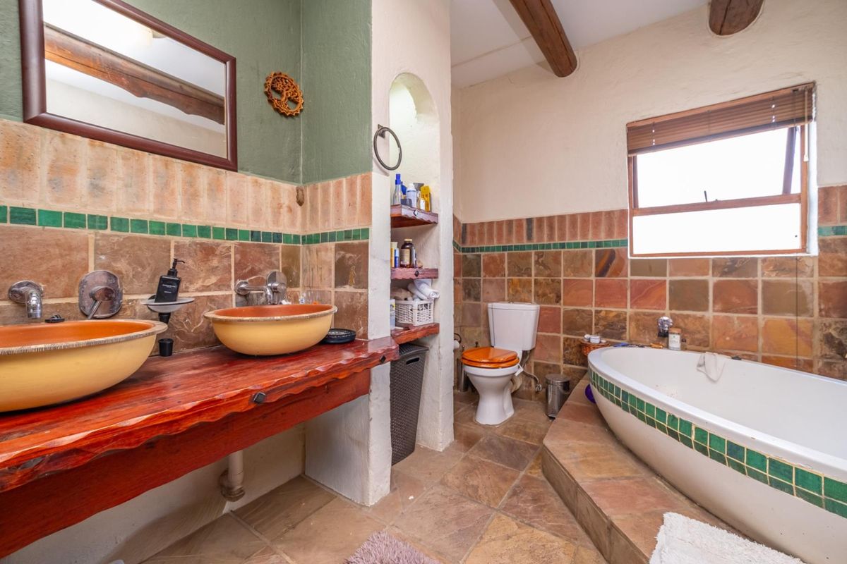 A rustic-style bathroom featuring dual vessel sinks on a wooden vanity, a built-in bathtub, and a toilet, finished with natural stone wall and floor tiles.