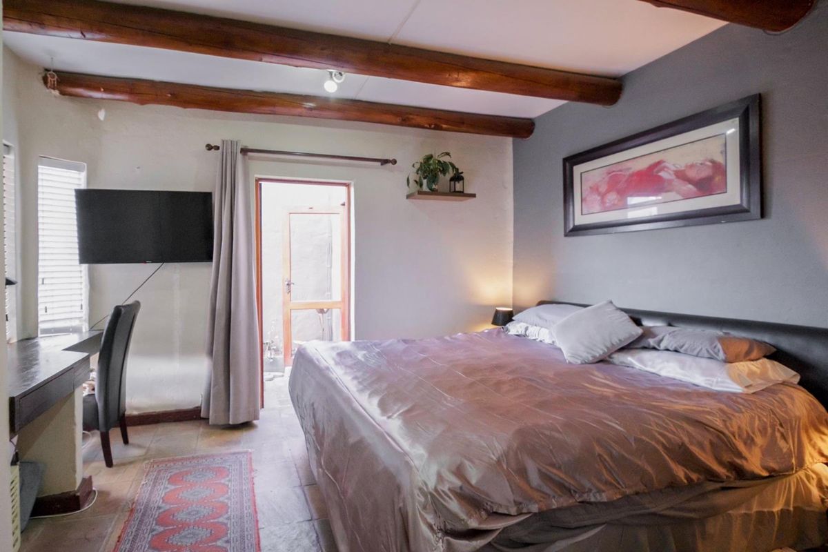 A bedroom featuring exposed timber ceiling beams, tiled flooring, and direct access to an outdoor area through a glass-paneled door.