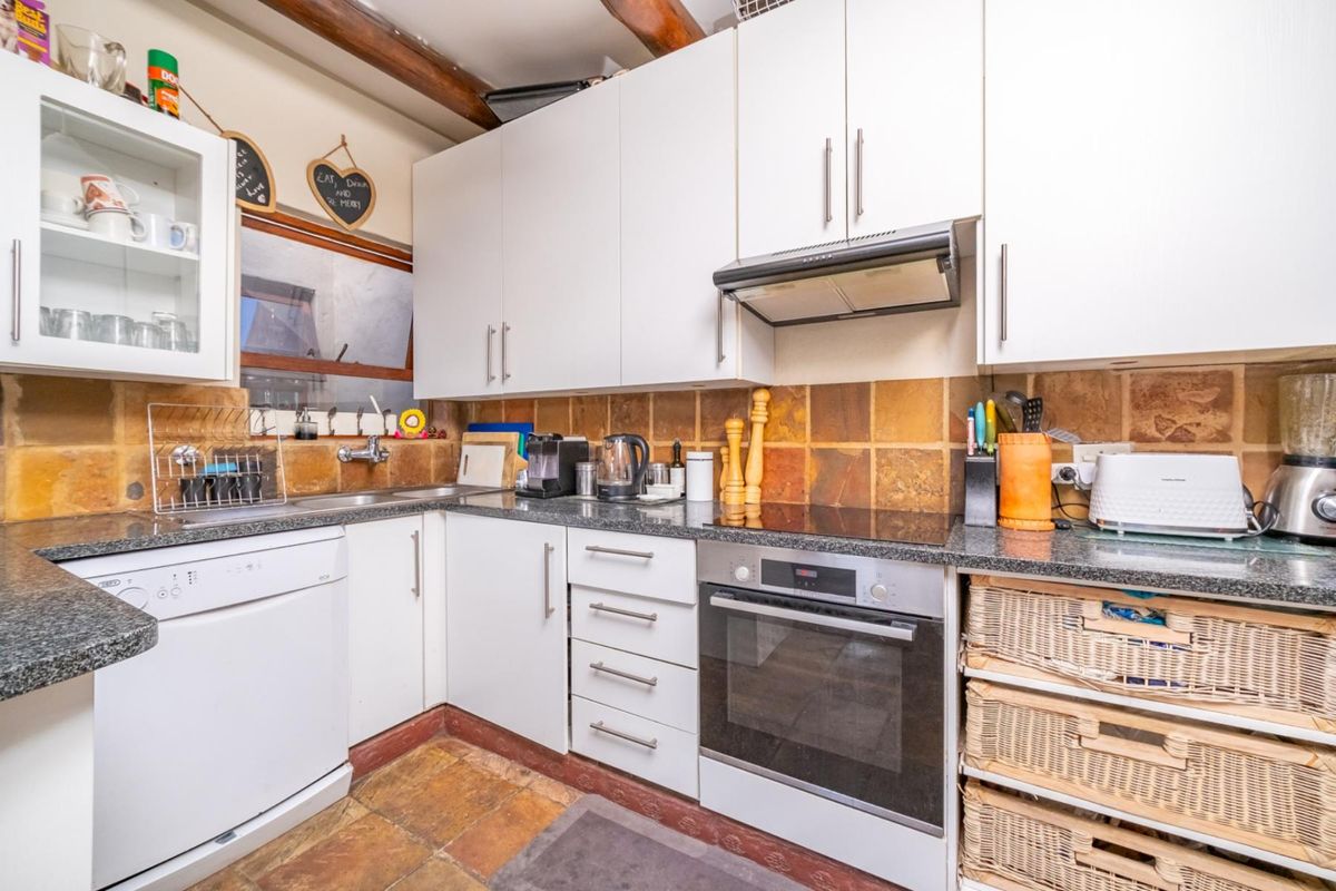 A functional kitchen featuring white cabinetry, granite-look countertops, a built-in oven, extractor fan, and rustic stone-style floor and wall tiling.