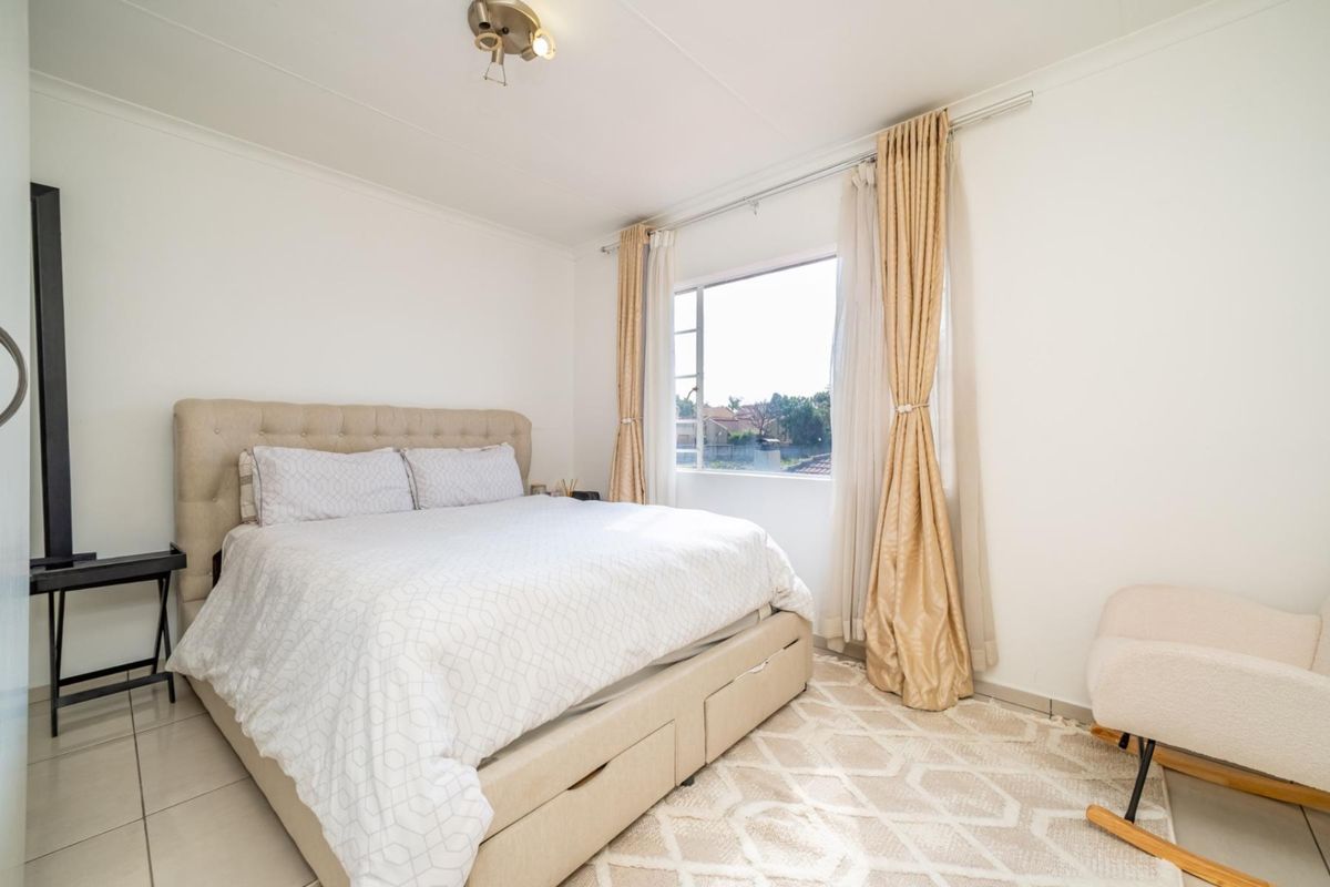 A bright and well-maintained bedroom featuring neutral tiled flooring and large windows with installed curtain tracks.