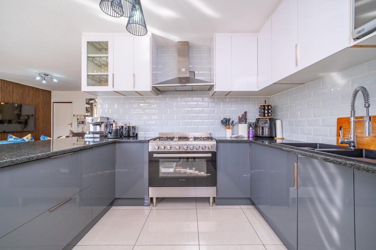 Modern kitchen featuring high-gloss grey cabinetry, granite countertops, subway tile backsplash, and a stainless steel gas stove with extractor fan.
