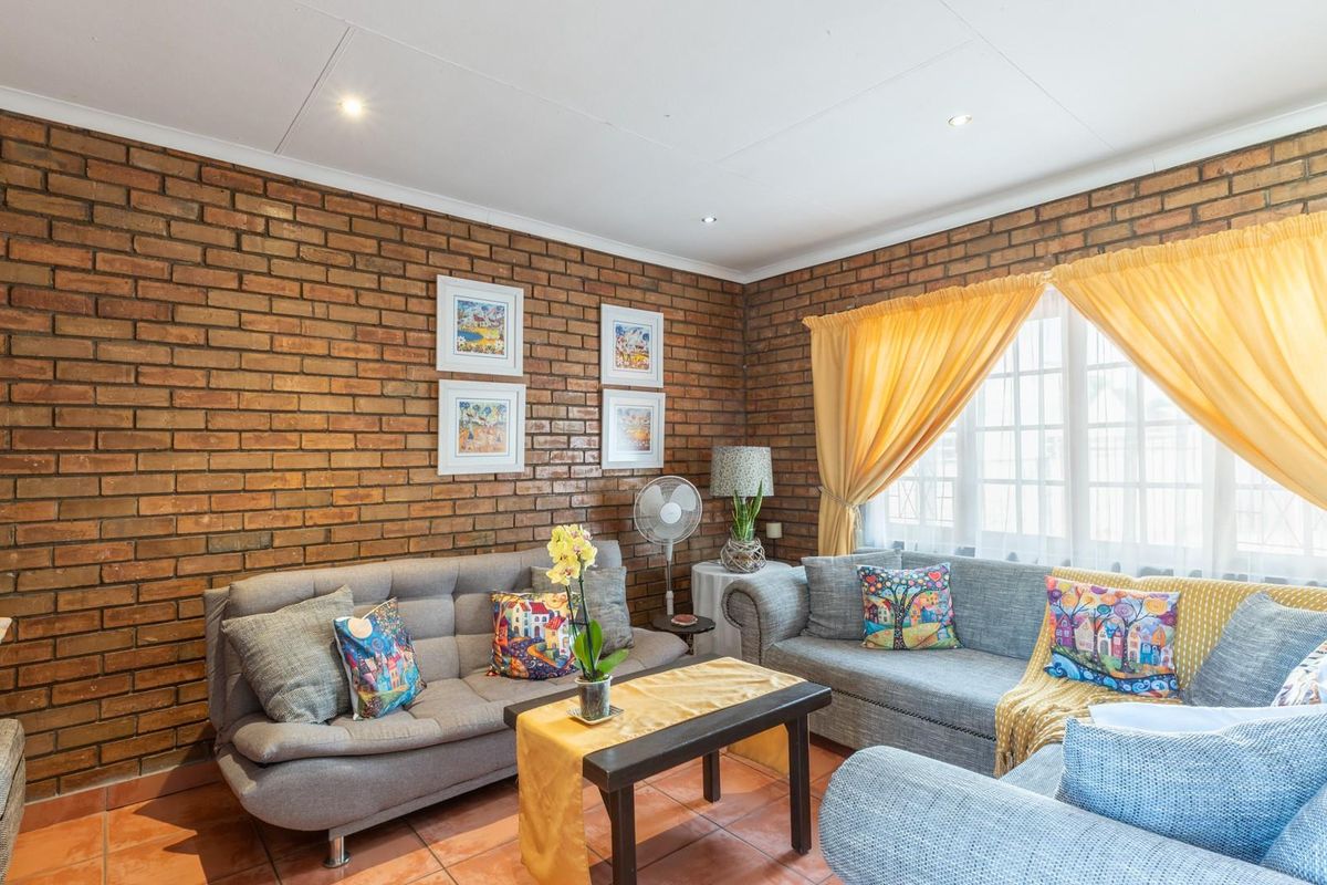 A cozy living room featuring a prominent exposed face-brick feature wall, tiled flooring, and large windows allowing for natural light.