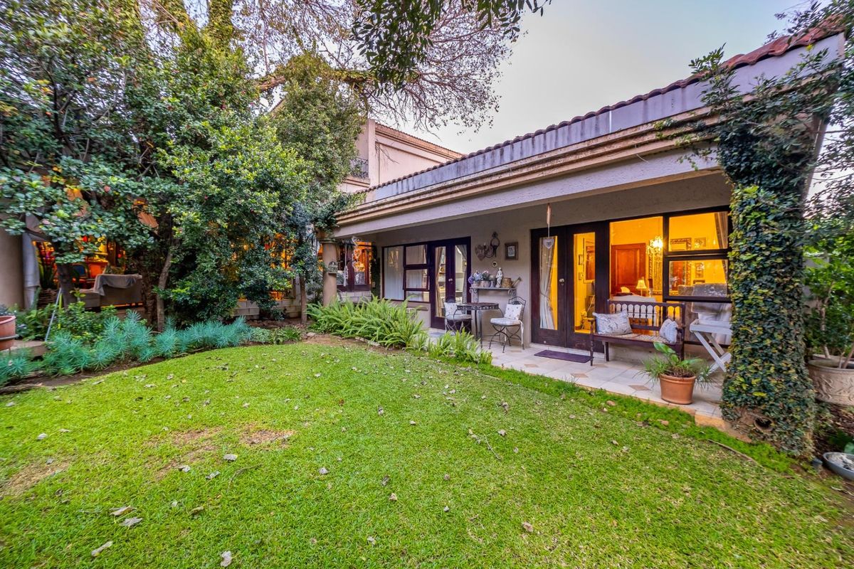A rear view of the property featuring a covered patio area, tiled flooring, and direct access to a lush, established garden with mature trees.