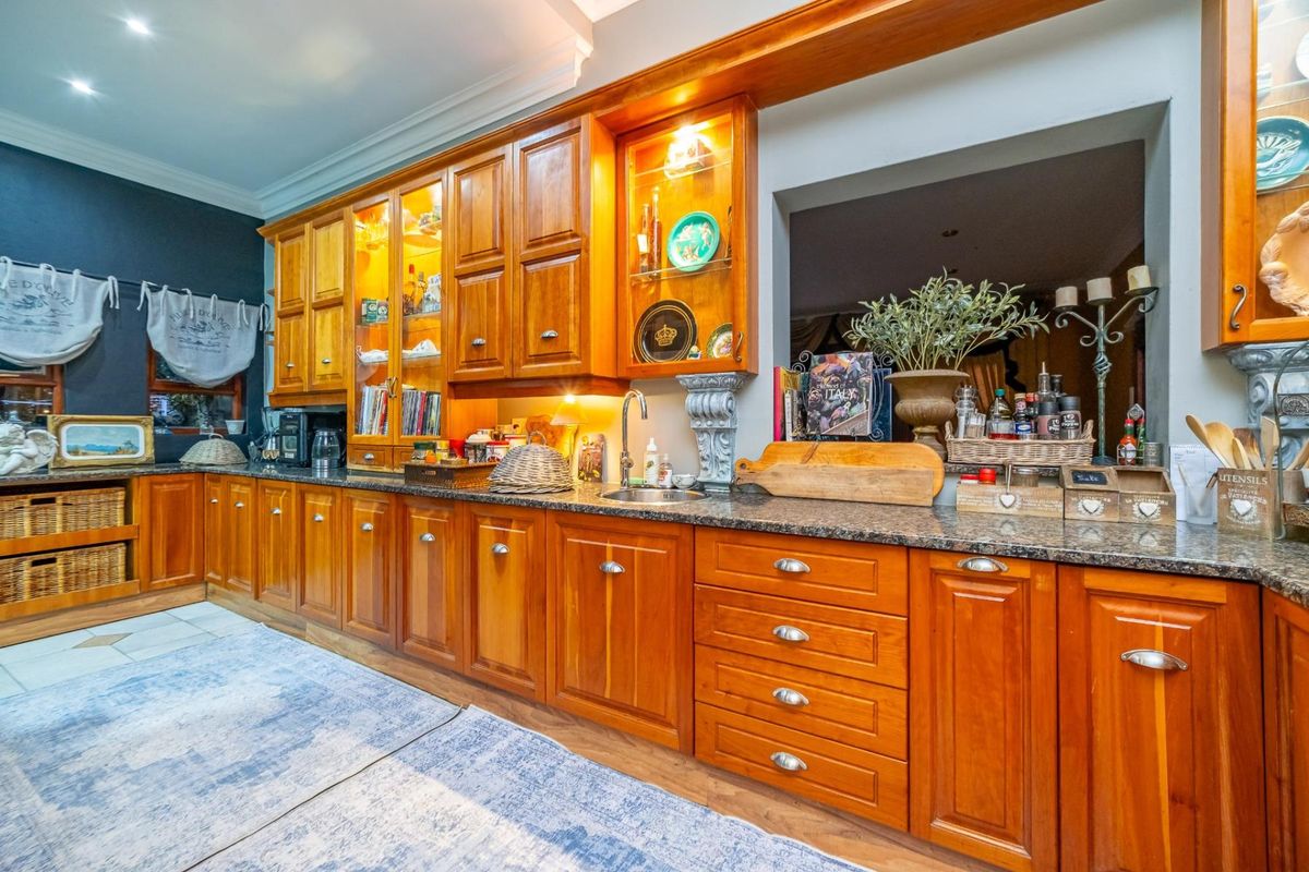 A traditional kitchen featuring extensive wooden cabinetry, granite countertops, an undermount sink, and integrated display shelving with built-in lighting.