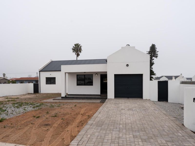 Front elevation of a modern single-story house featuring a paved driveway, integrated garage, and a clean white facade with a dark metal roof.