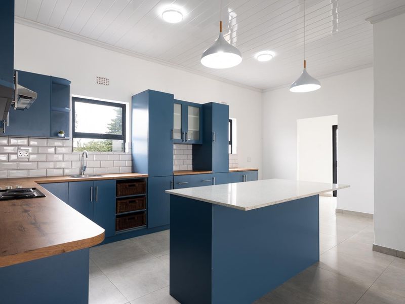 Modern kitchen featuring blue cabinetry, a central island with stone countertop, subway tile backsplash, and integrated gas hob with extractor fan.
