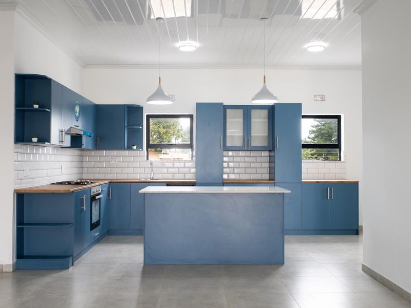 Modern kitchen featuring blue cabinetry, timber countertops, a central island, subway tile backsplash, and a distinctive tongue and groove ceiling.