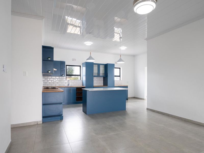 Modern kitchen featuring blue cabinetry, a central island, wooden countertops, subway tile backsplash, and sleek tiled flooring in an open-plan layout.