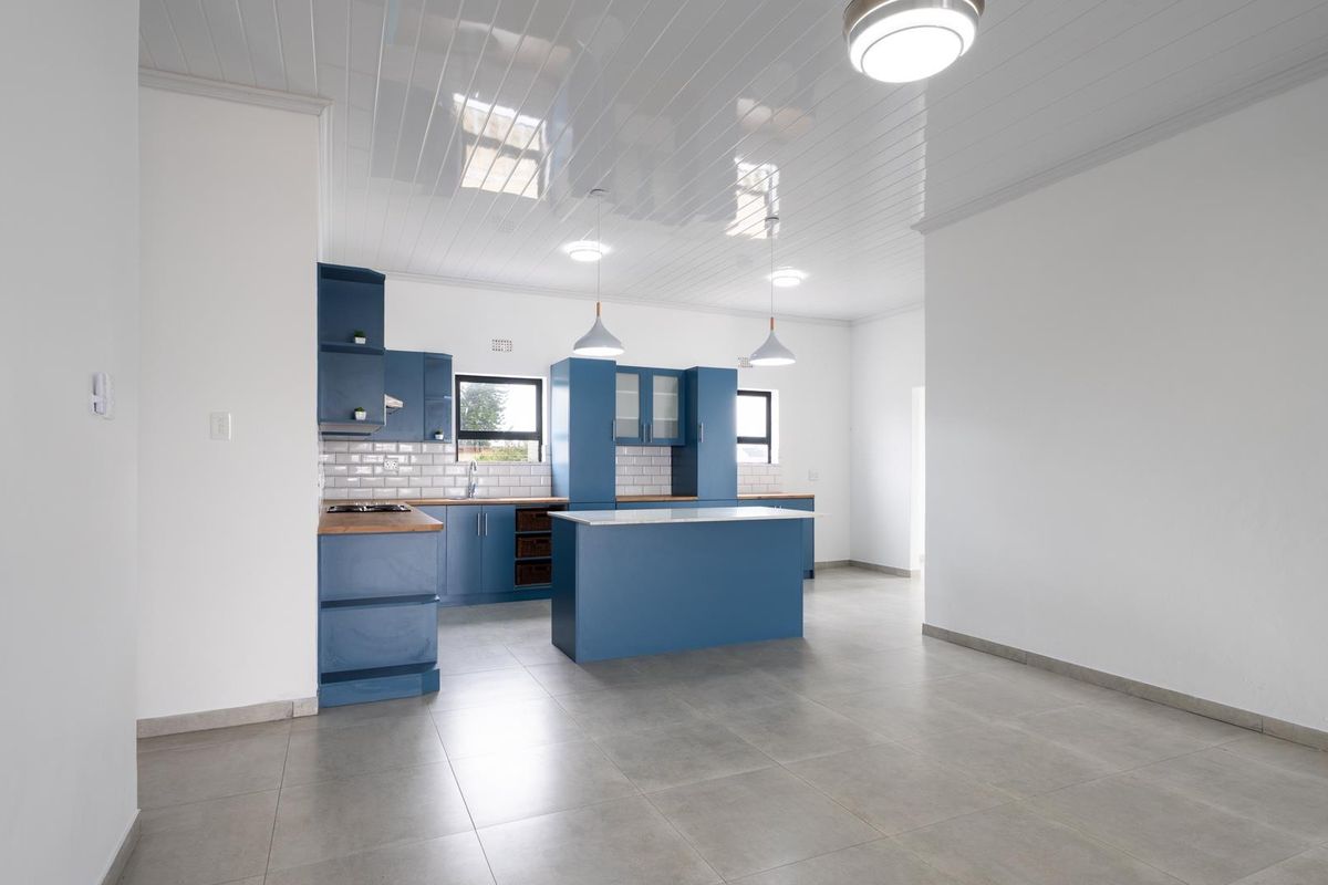 Modern kitchen featuring blue cabinetry, a central island, wooden countertops, subway tile backsplash, and sleek tiled flooring in an open-plan layout.