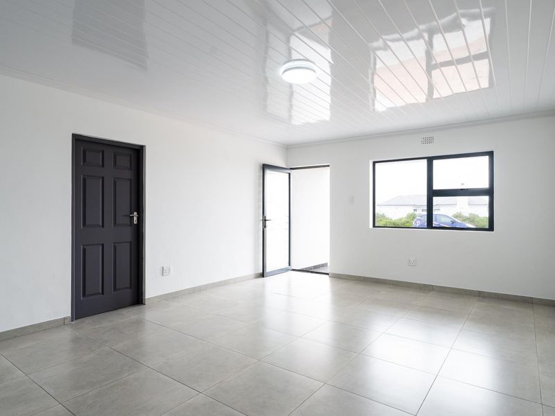A bright, empty living area featuring neutral floor tiles, a glossy ceiling finish, and modern aluminium window frames.
