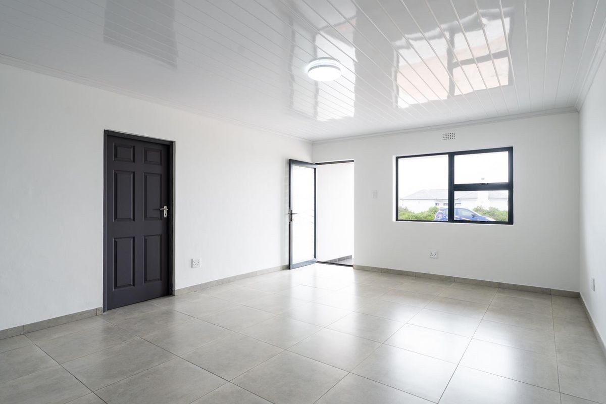 A bright, empty living area featuring neutral floor tiles, a glossy ceiling finish, and modern aluminium window frames.