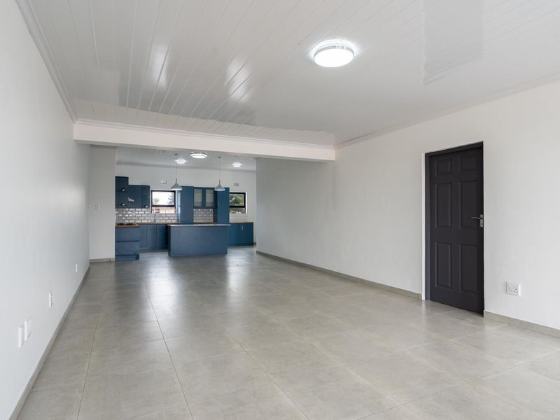 Spacious open-plan living area featuring neutral tiled flooring, a modern blue kitchen with an island, and clean white walls.