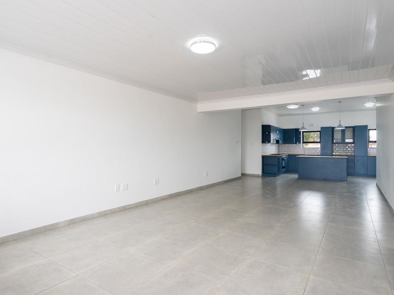 Spacious open-plan living area featuring neutral tiled flooring and a modern kitchen with blue cabinetry, a central island, and subway tile backsplash.
