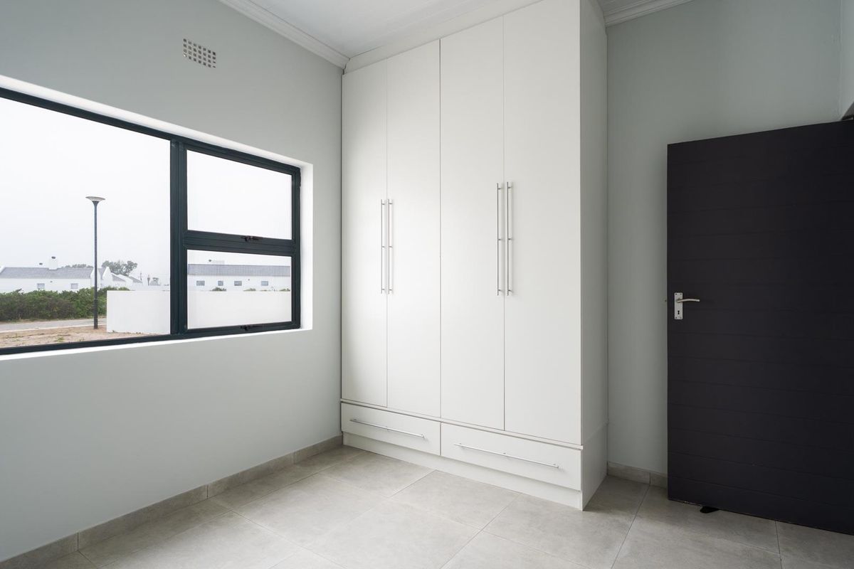 A bright, empty bedroom featuring neutral tiled flooring, a large built-in wardrobe, and modern aluminium-framed windows.