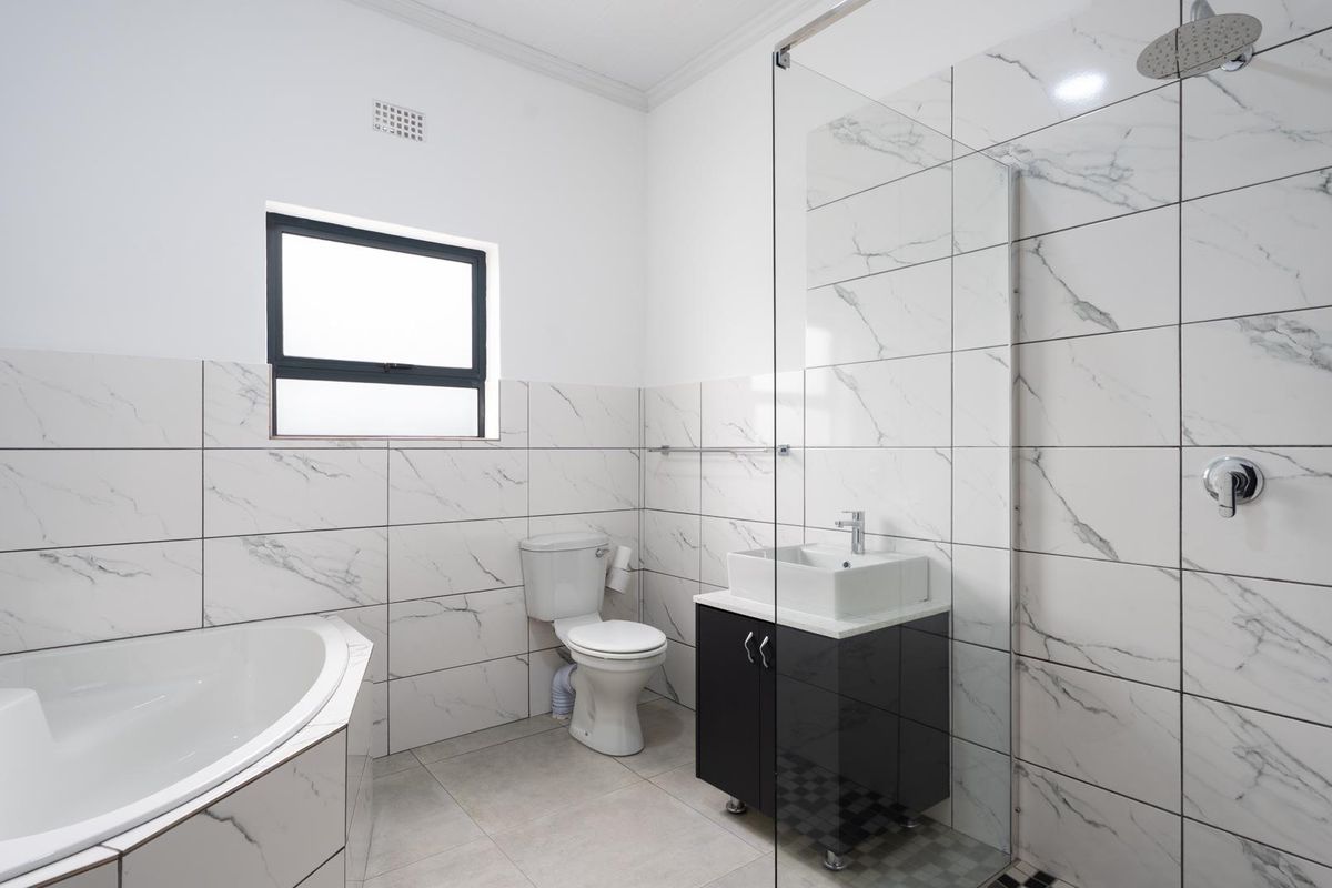 Modern bathroom featuring a corner bathtub, walk-in shower with glass screen, vessel sink vanity, and contemporary marble-look wall tiling.