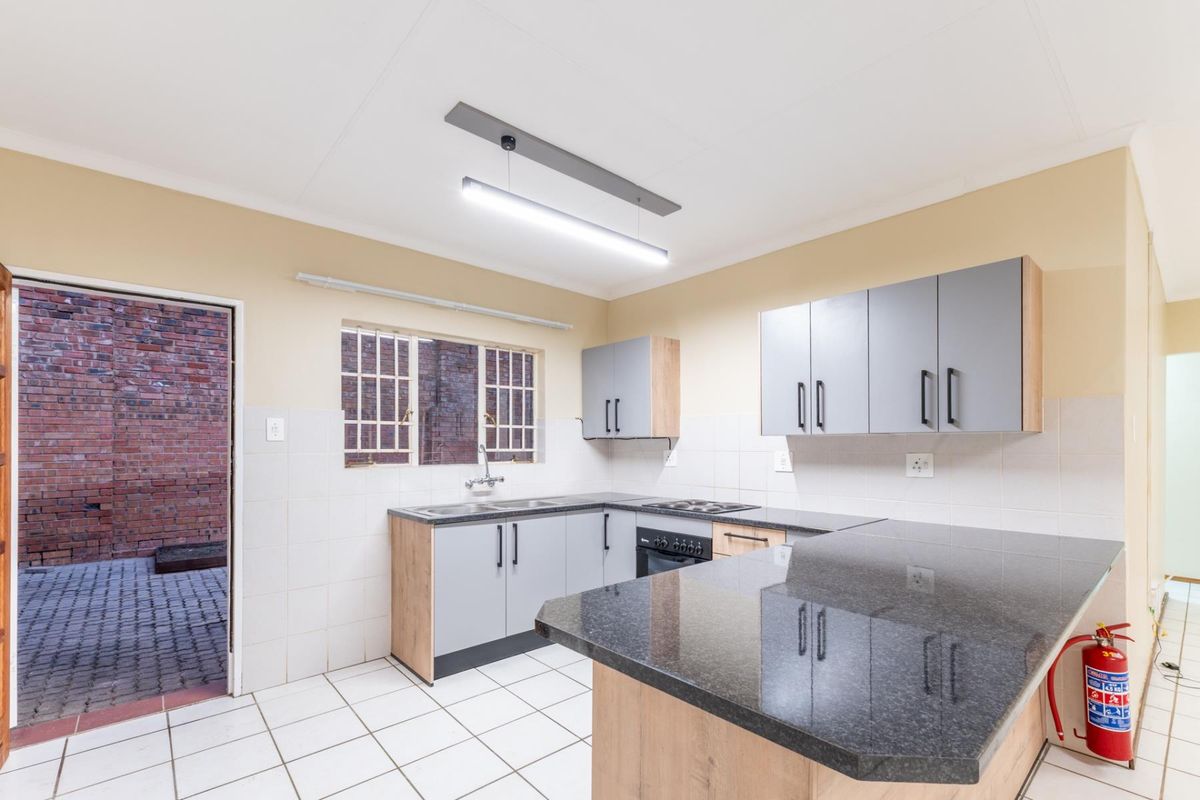 Modern kitchen featuring granite countertops, light wood cabinetry, built-in oven and hob, and direct access to a paved rear courtyard.