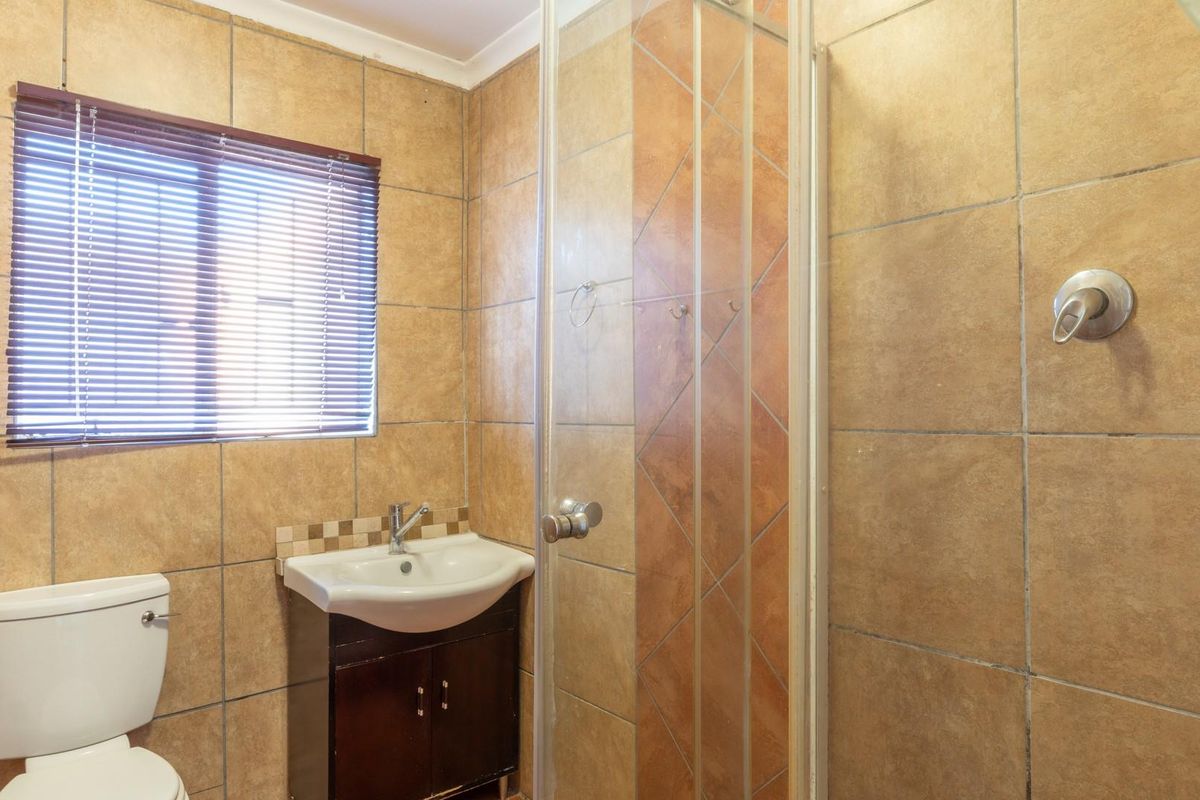 A functional bathroom featuring a glass-enclosed shower, a vanity basin, and a toilet, finished with neutral wall tiles.