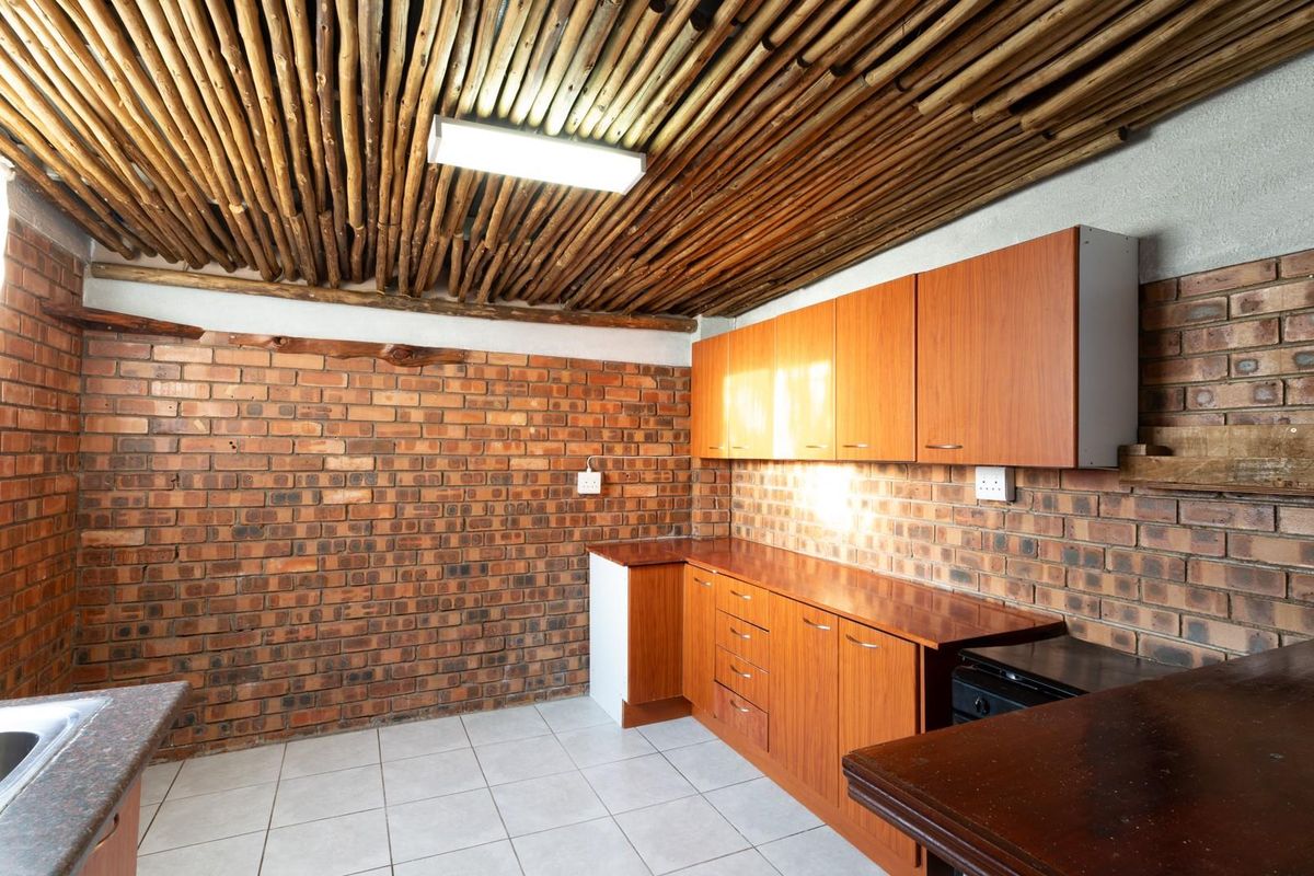 A functional kitchen featuring exposed brick walls, wooden cabinetry, tiled flooring, and a unique rustic timber-slat ceiling design.