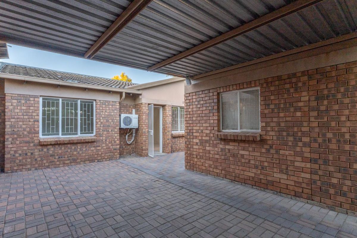 A paved courtyard area featuring a covered carport structure, face-brick exterior walls, and security-fitted windows.