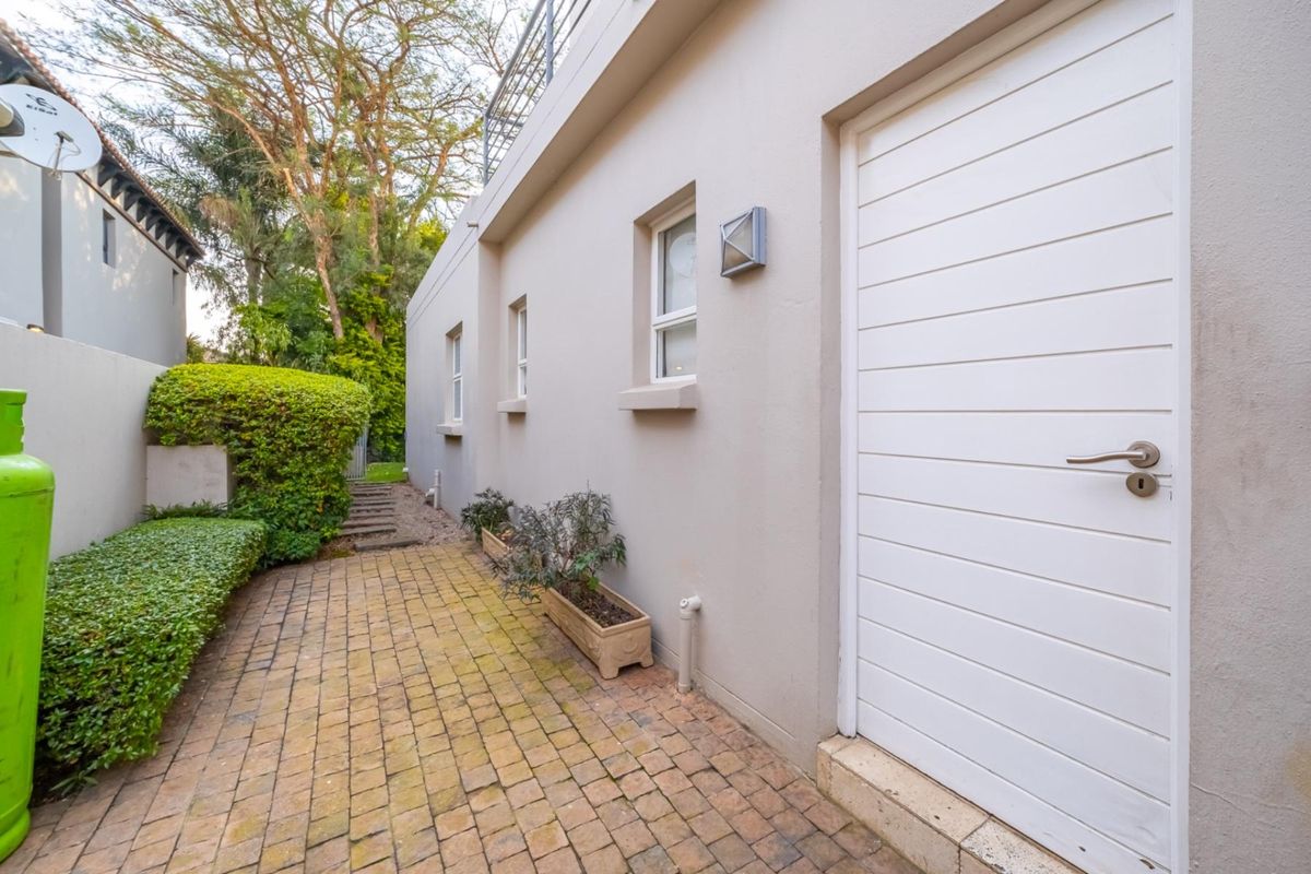 A side exterior view of the property featuring a paved walkway, white door, and landscaped garden area.