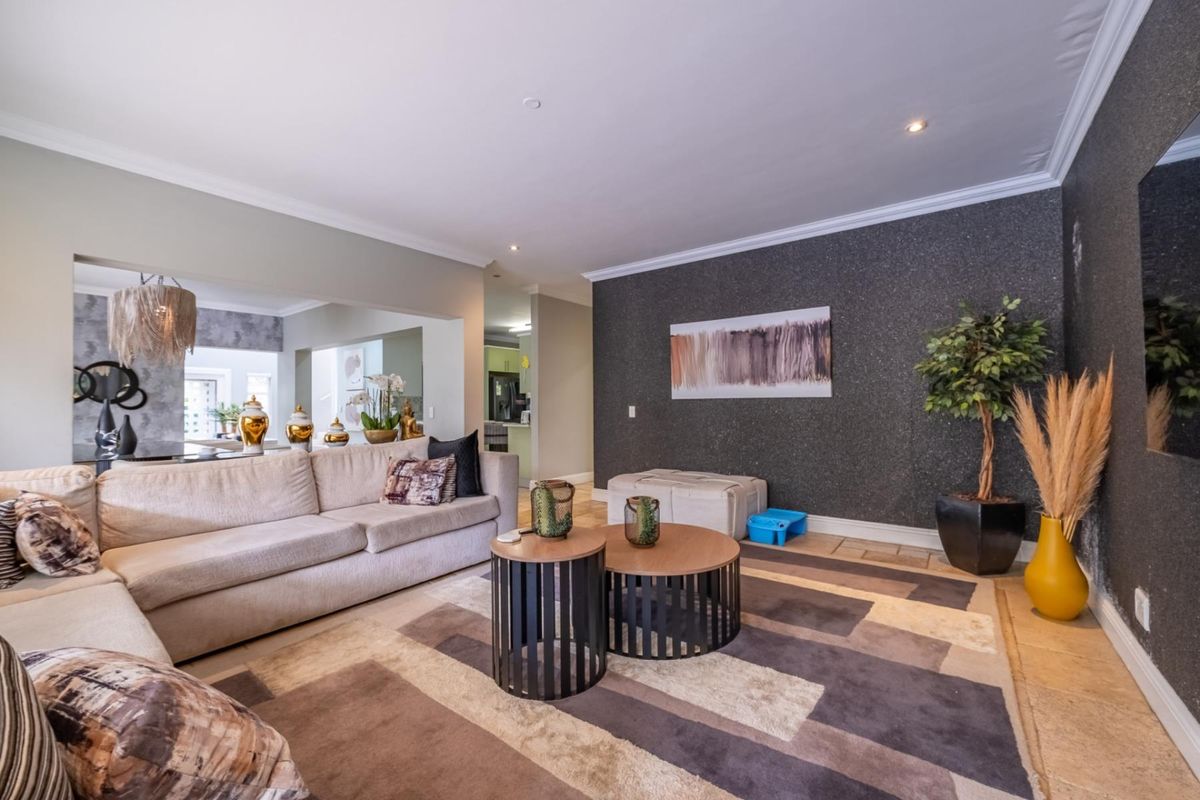 Spacious living room featuring a textured feature wall, recessed lighting, and tiled flooring, with an open-plan flow into the adjacent kitchen area.