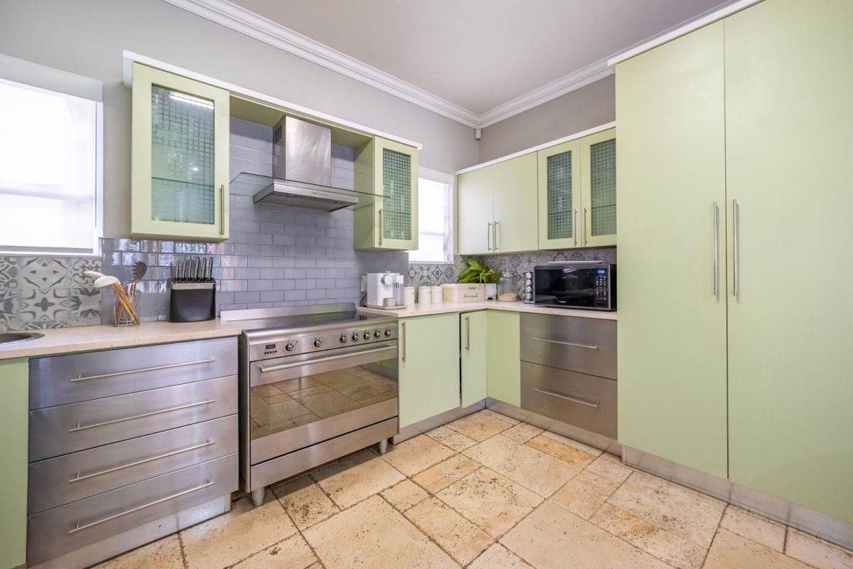 A well-maintained kitchen featuring light green cabinetry, stainless steel appliances, a subway tile backsplash, and natural stone flooring.