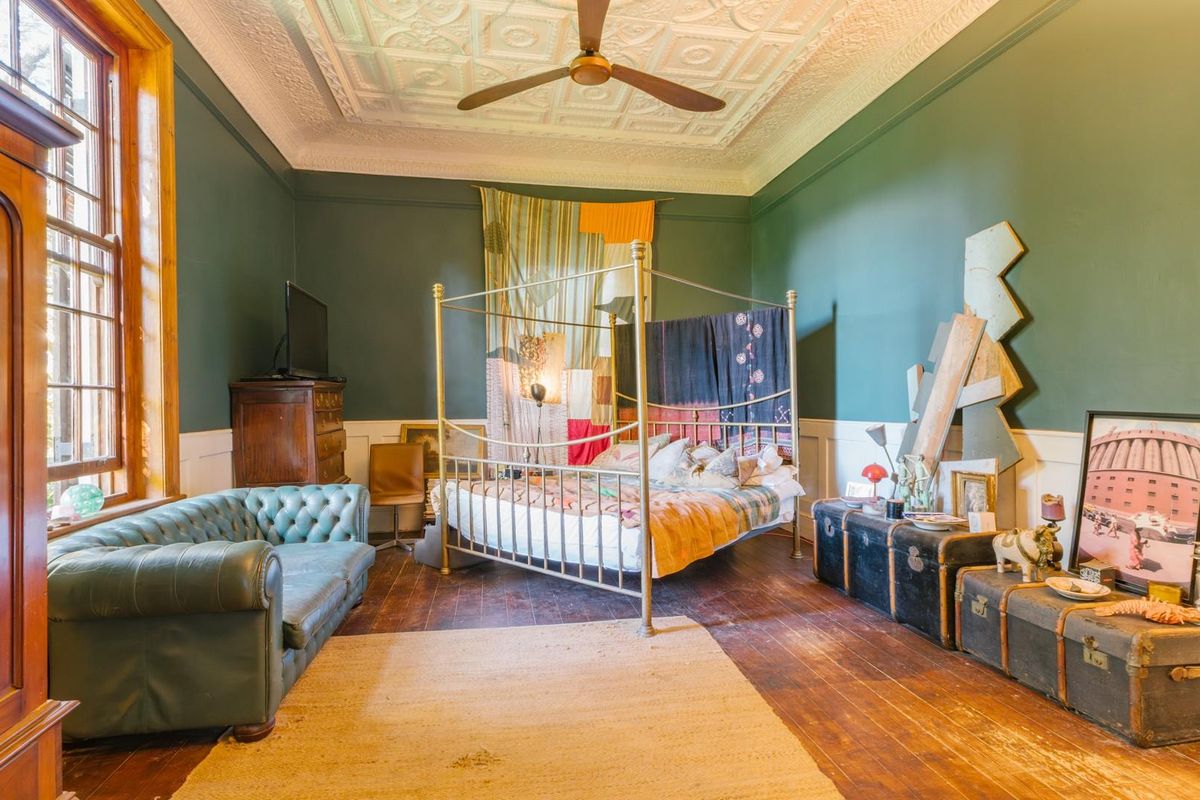 Spacious bedroom featuring high ceilings with decorative pressed metal detailing, timber flooring, and large sash windows.